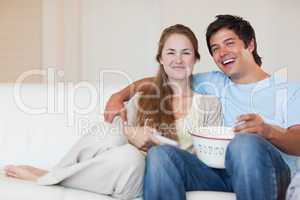 Smiling couple watching television while eating popcorn