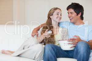 Charming couple watching television while eating popcorn