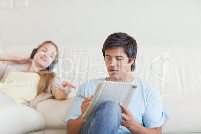Woman helping her fiance to do crosswords while listening to mus