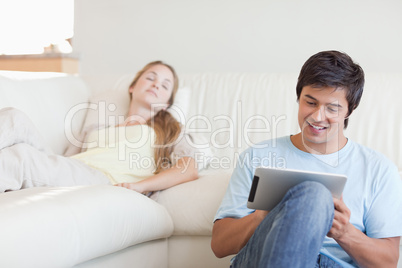 Young man using a tablet computer while his girlfriend is sleepi