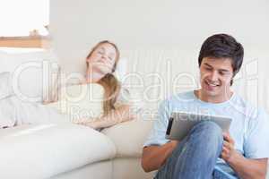 Young man using a tablet computer while his girlfriend is sleepi