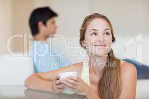 Woman having a tea while her fiance is sitting on a sofa