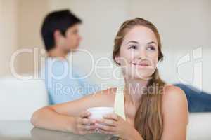 Woman drinking coffee while her fiance is sitting on a couch