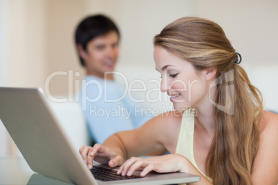 Woman using a laptop while her husband is sitting on a sofa