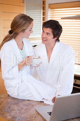 Portrait of a charming couple having breakfast while using a lap