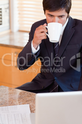 Portrait of a businessman drinking coffee while using a laptop