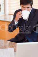Portrait of a businessman drinking coffee while using a laptop