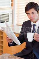 Portrait of a businessman drinking tea while reading a newspaper