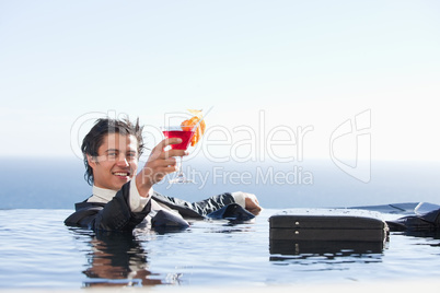 Cheerful businessman relaxing in a swimming pool with a cocktail