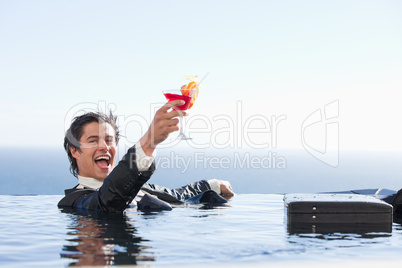 Delighted businessman relaxing in a swimming pool with a cocktai