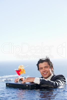 Portrait of a businessman relaxing in a swimming pool with a coc