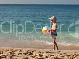Child boy holding ball on sea sand beach