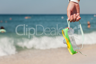 Hand holding diving goggles on sea beach