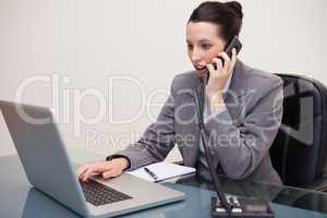 Businesswoman typing on laptop while talking on the phone