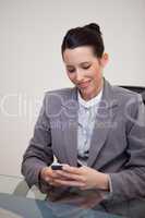 Smiling businesswoman sitting behind desk writing a textmessage