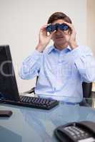 Businessman looking through binoculars in his office