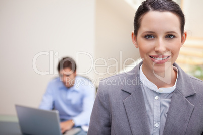 Smiling businesswoman with colleague working on his laptop behin