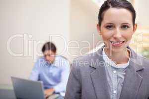 Smiling businesswoman with colleague working on his laptop behin
