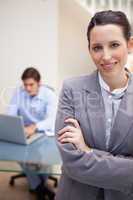 Smiling businesswoman with colleague on his laptop behind her