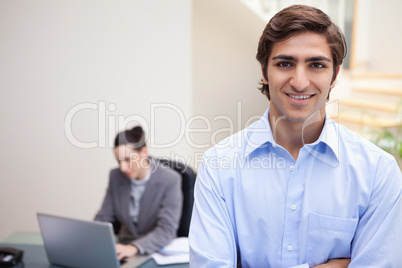 Smiling businessman with colleague on her laptop behind him