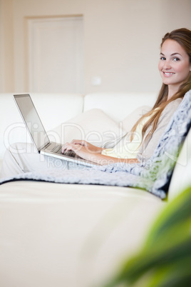 Side view of smiling woman with her laptop sitting on the sofa