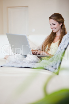 Side view of smiling woman working on her laptop on the sofa