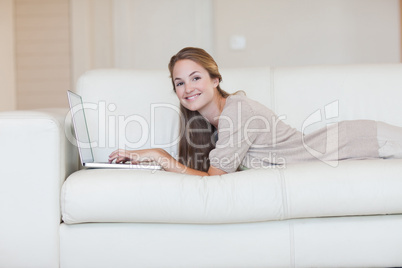 Side view of woman lying on her sofa with her laptop