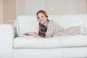 Side view of woman lying on her sofa with her laptop