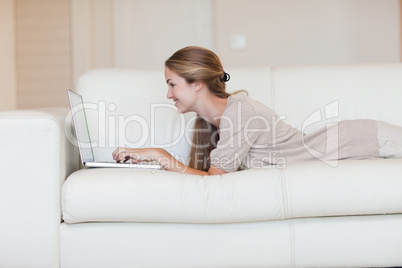 Side view of woman lying on the couch working on her laptop