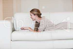 Side view of woman lying on the couch working on her laptop