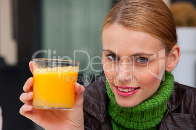young woman holding a glass of orange juice and looking at camer