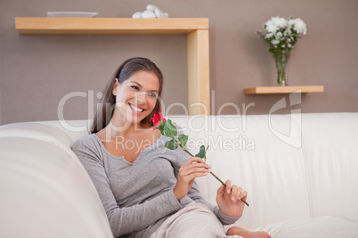 Smiling woman with a red rose sitting on the sofa