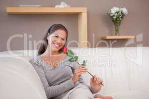 Smiling woman with a red rose sitting on the sofa