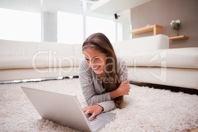 Smiling woman lying with laptop on the floor