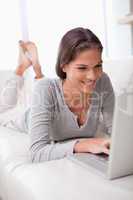 Smiling woman lying on the sofa with her laptop