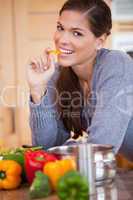 Smiling woman eating a bell pepper in the kitchen