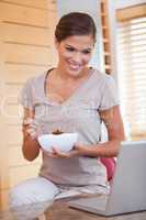 Woman eating cereals while looking at her laptop