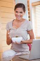 Smiling woman eating cereals next to her laptop