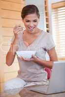 Woman eating cereals next to her laptop