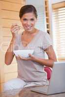 Woman having a bowl of cereals next to her laptop