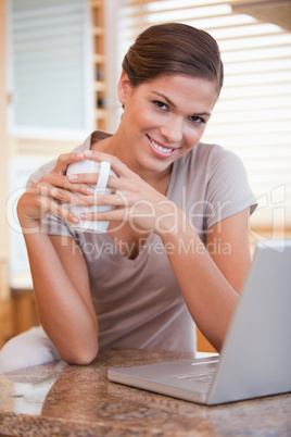 Smiling woman with coffee and laptop in the kitchen