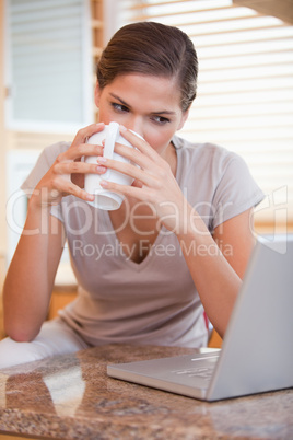 Woman taking a sip of coffee next to her laptop