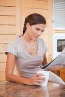 Woman reading newspaper while holding cup of coffee