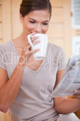 Woman taking a sip of coffee while reading newspaper