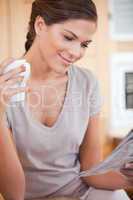 Woman reading newspaper while holding cup of tea