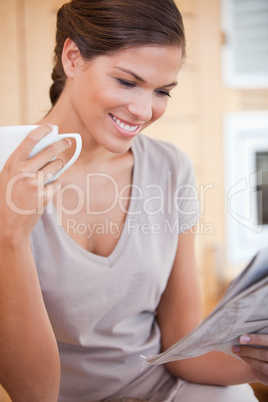 Smiling woman reading newspaper while having tea