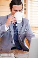 Businessman taking a sip of coffee next to his laptop