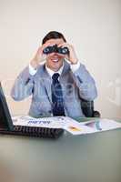 Businessman at his desk looking through binoculars