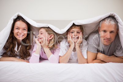 Happy family lying under a duvet