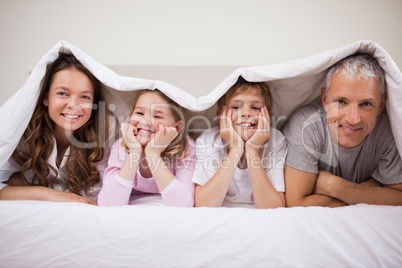Playful family lying under a duvet
